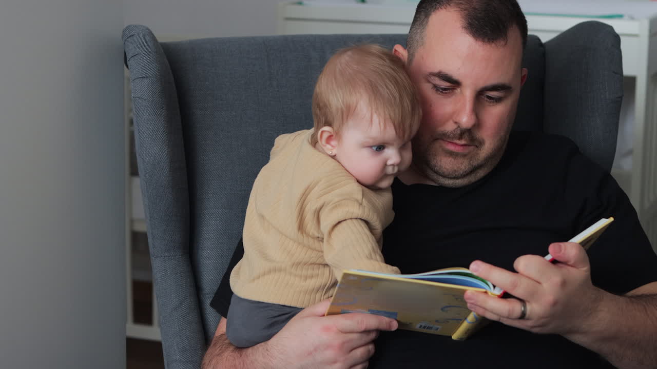 Father reading story to his baby daughter while she looks intently at book