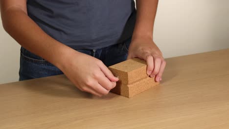 Hands manipulate a wooden block with a hook and screw on a table. Neutral lighting, close-up focus