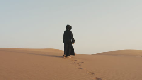 Vista-Trasera-De-Una-Mujer-Musulmana-Irreconocible-Con-Hijab-Caminando-Descalza-En-Un-Desierto-Ventoso