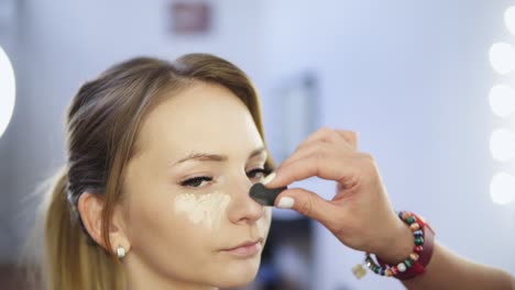 primer plano de un artista de maquillaje profesional aplicando corrector a la piel de una mujer joven con pincel para cubrir las ojeras y hacer que la cara se vea más brillante. filmado en 4k