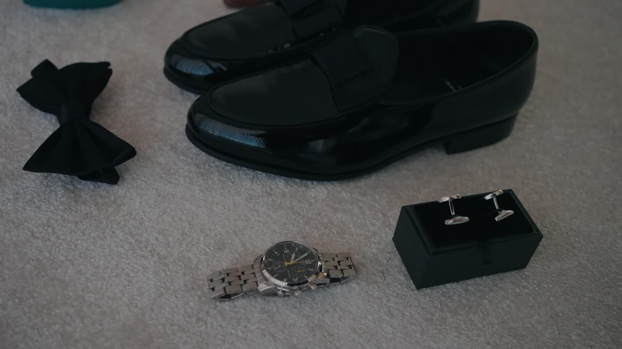 바닥에 놓인 우아한 신랑의 에센셜 슈즈, 시계, 커프스 단추, 보타이