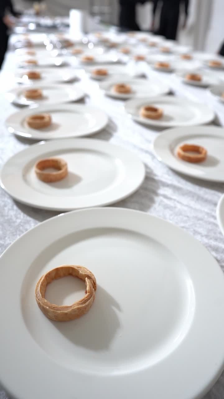 Minimalist fine dining setup with white plates arranged in rows, each holding a small pastry, close up shot