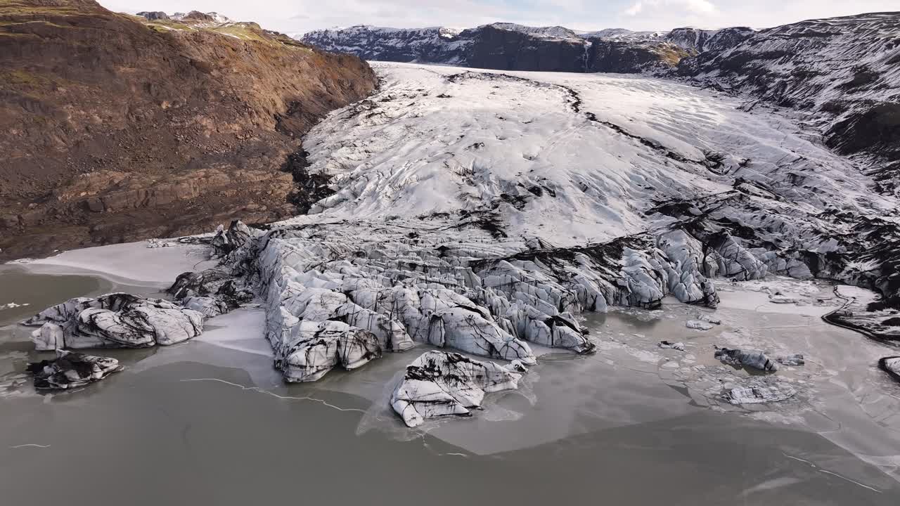 Drone flying over Sólheimajökull glacier in Iceland, capturing stunning icy formations, deep crevasses, and melting ice blending into a frozen lagoon.