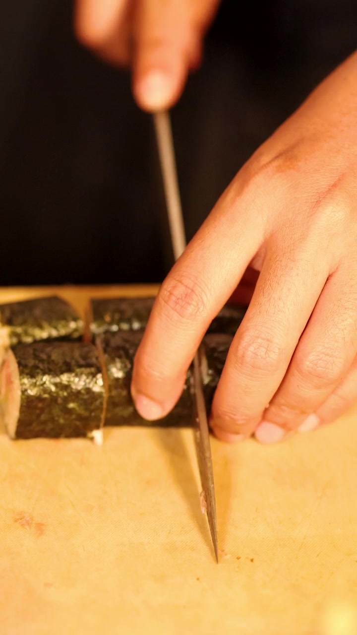 Detailní záběr na šéfkuchaře krájícího tuňákovou maki rolku a opatrně ji servírujícího na talíř.