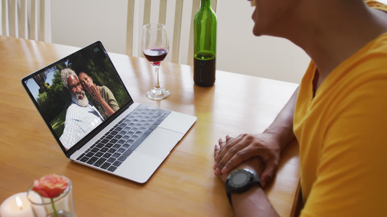 Mid section of african american man with wine while having a video call on laptop at home