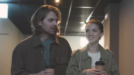 pareja feliz con bebidas para llevar riendo y caminando juntos en el cine