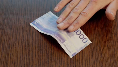 hand placing norwegian 1000 kr note in center of wooden table