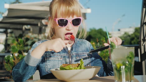 Una-Niña-Con-Gafas-De-Color-Rosa-Está-Comiendo-Una-Ensalada-En-El-Patio-De-Verano-De-Una-Cafetería-De-Vacaciones-De-Verano-Con-Niños