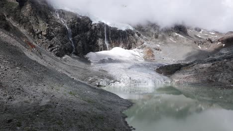 Fellaria-Glacier-tongue-and-lagoon-with-rocky-mountains-shrouded-in-clouds-in-background,-Valmalenco-in-Italy