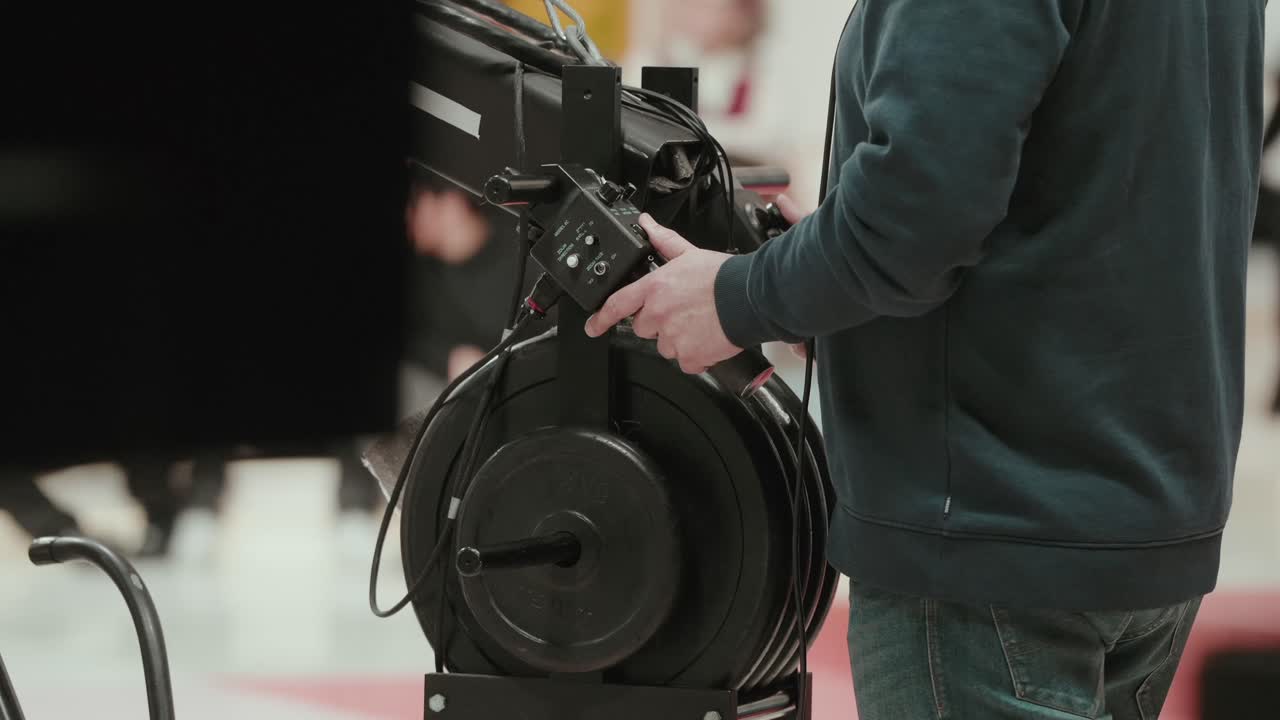 Crew member adjusting cable reel on studio camera crane during setup