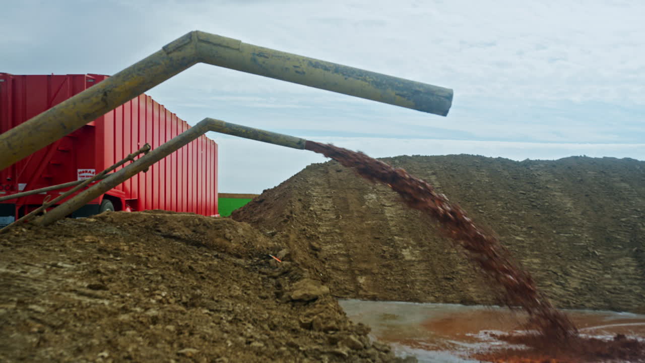 Two pipes over the ground pile, one of which produces a flow of muddy liquid. Site for oil or gas production.