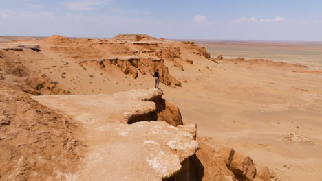 Bayanzag-Flaming-Cliffs-With-Man-Standing-On-Edge-Of-The-Cliff-In-Mongolia---Aerial-Drone-Shot