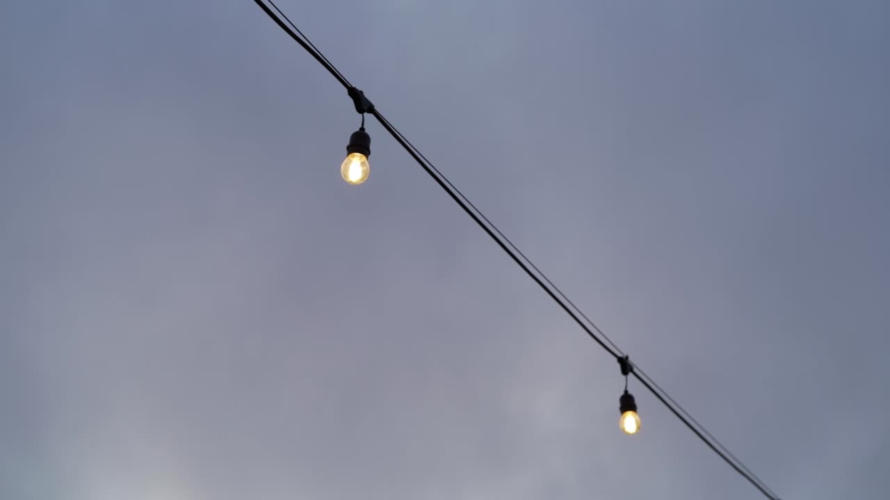 Guirlande lumineuse avec ampoules brillantes suspendue à l'extérieur sous un ciel couvert.