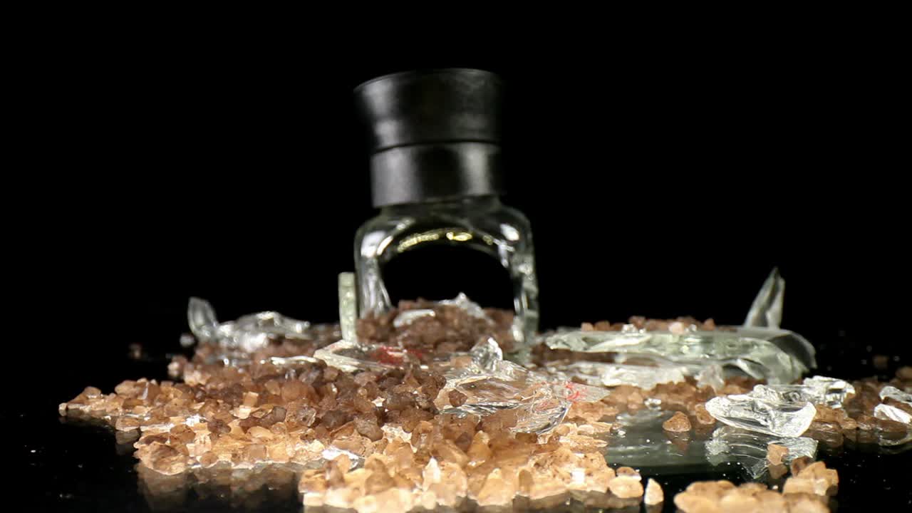 Lento avvicinamento a un macinasale marino rotto, con la parte superiore in posizione verticale, vista macro grandangolare - che mostra una maggiore quantità di sale e alcuni frammenti di vetro rotto mescolati