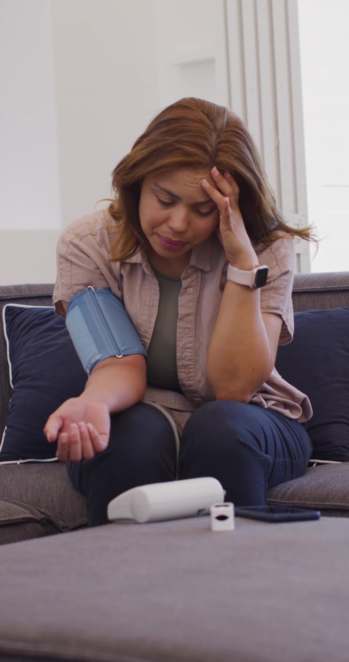 Video verticale: Donna afroamericana che posiziona il bracciale sul braccio sinistro sul divano controllando le letture del monitor