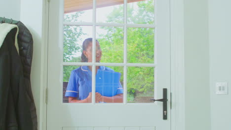 senior woman greeting female nurse or care worker making home visit in uniform at door