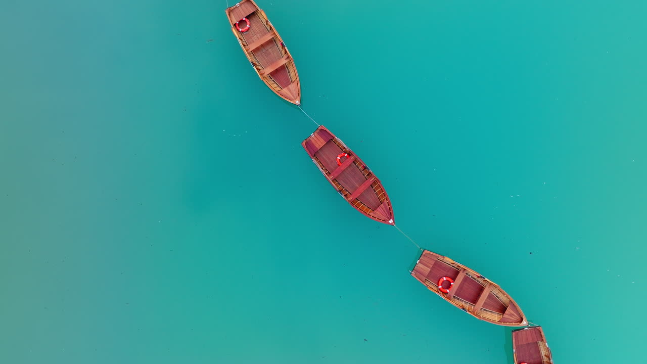 Overhead view of red wooden rowboat floating attached in line on Dolomites lake Braies in quiet natural light