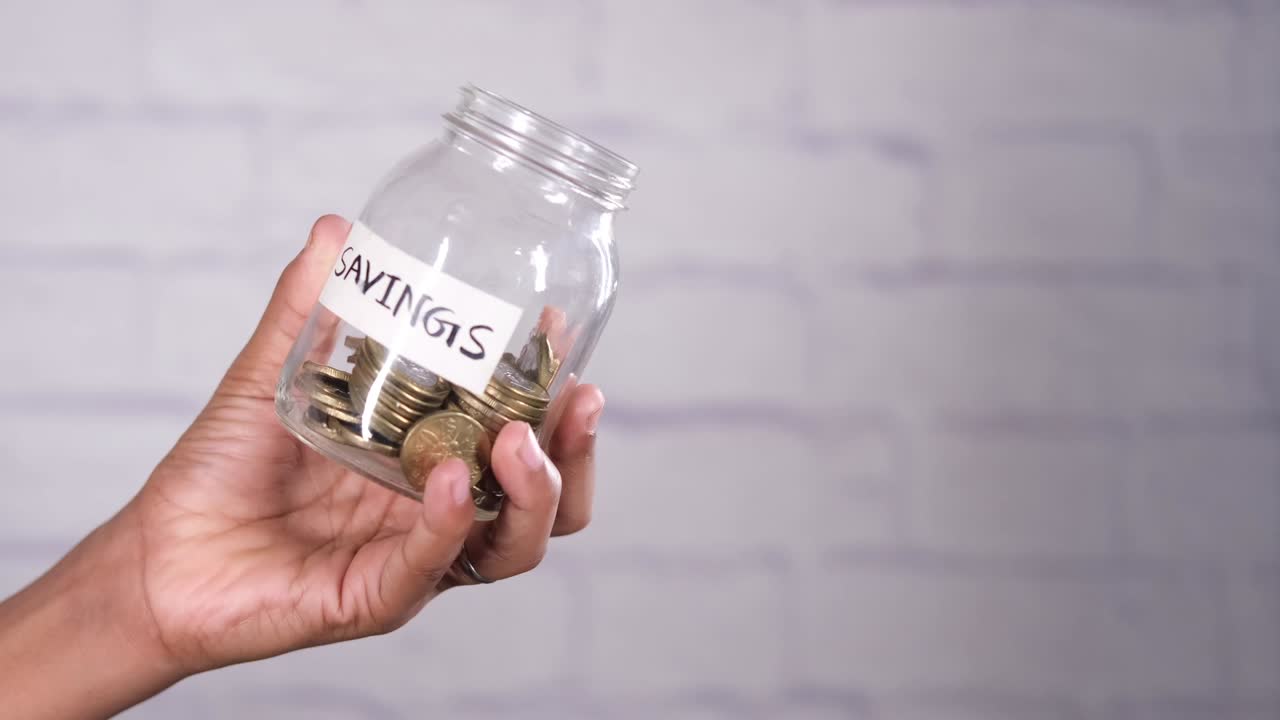young man hand hold saving coins jar