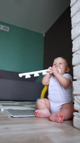 lovely plump baby boy with fair hair sits on the floor. little kid is teething so pull stuff to his mouth. vertical video.