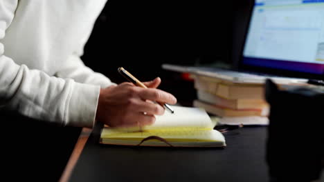 junger, moderner kaukasischer mann, der sich notizen macht und pläne schmiedet, indem er kreative ideen in sein notizbuch schreibt, während er erfolgreich an einem professionellen studio arbeitet