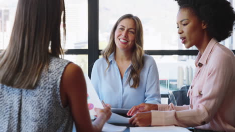 Female-Multi-Cultural-Business-Team-Meet-Around-Boardroom-Table-With-Laptops-Discussing-Documents