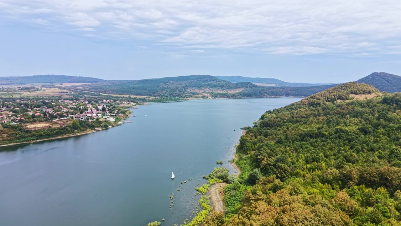 Vista del fiume che serpeggia tra colline e alberi con una piccola barca che naviga sotto un cielo nuvoloso in campagna