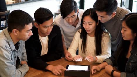 a group of friends engaging around a tablet in a cozy cafe environment, sharing ideas and collaborating on a project with focused attention and enthusiasm