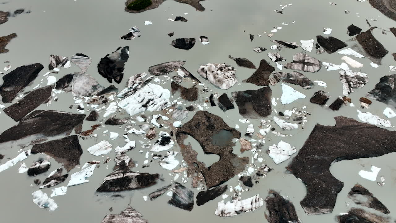Approaching the boulders of ice in the river with grey water. Ice melting in Alaska, USA. Aerial view