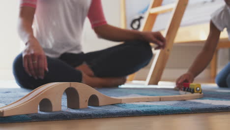 Close-Up-Of-Hispanic-Mother-And-Daughter-Playing-With-Toy-Train-Set-In-Bedroom-Together