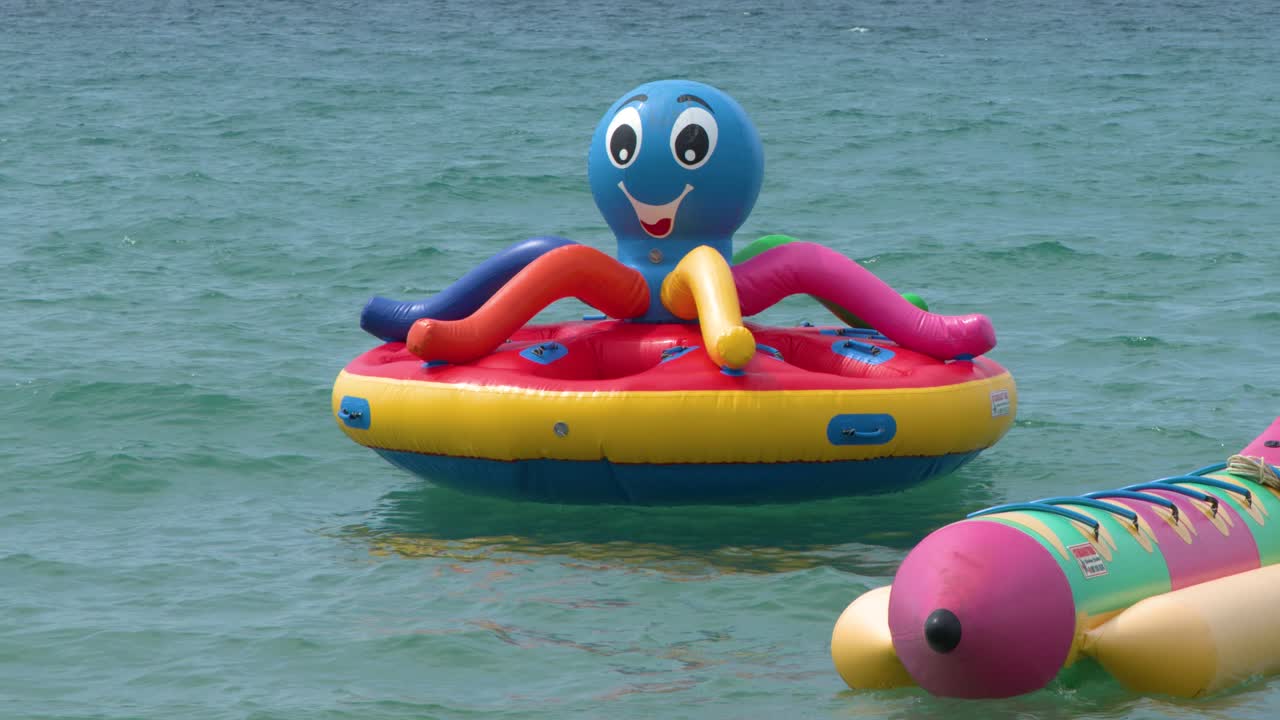 Static wide shot of vibrant inflatable water sports equipment floating on calm turquoise sea water