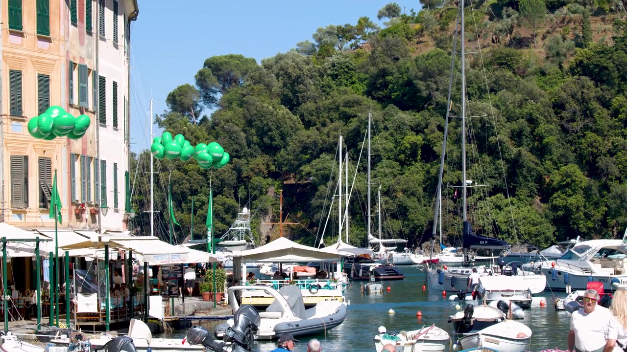 Ampia inquadratura fissa di un porto turistico mediterraneo con yacht, edifici colorati e palloncini verdi