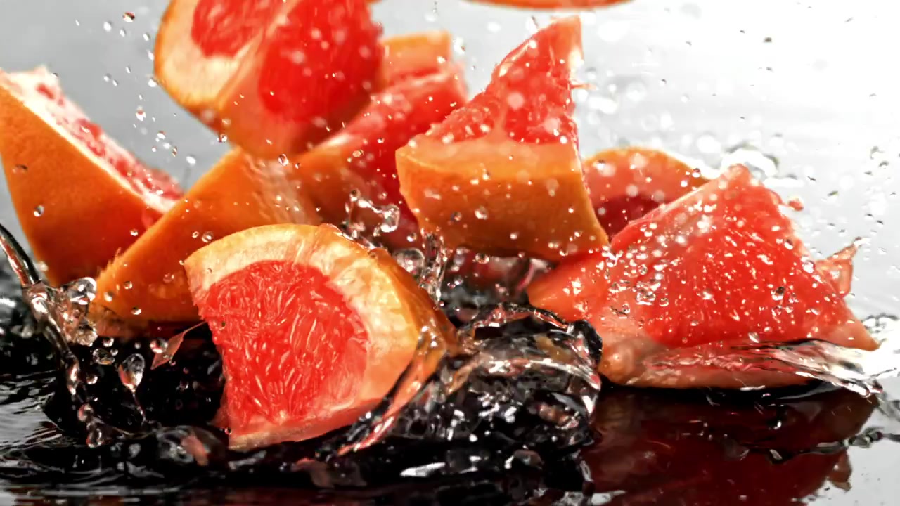 Frische Grapefruitscheiben spritzen in Zeitlupe ins Wasser
