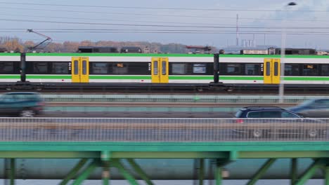 green and yellow modern train crossing a city bridge