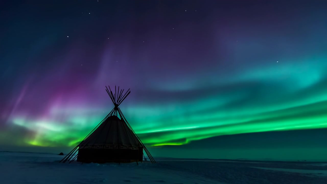 Silhouette centrata a sinistra di una tenda conica con pali a vista su una piana innevata sotto un'ampia aurora verde e verde acqua, stelle lontane, orizzonte luminoso e un vasto cielo notturno su una remota natura selvaggia polare.