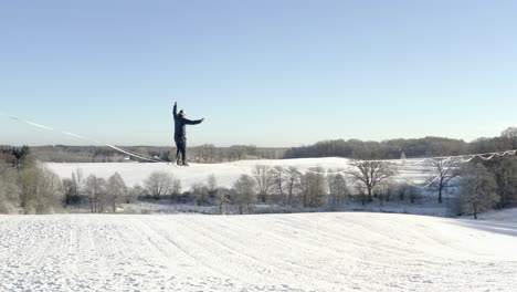 Un-Hombre-Caminando-Sobre-Una-Larga-Línea-Floja-En-Lo-Alto-De-Un-Campo-Cubierto-De-Nieve---Durante-El-Día