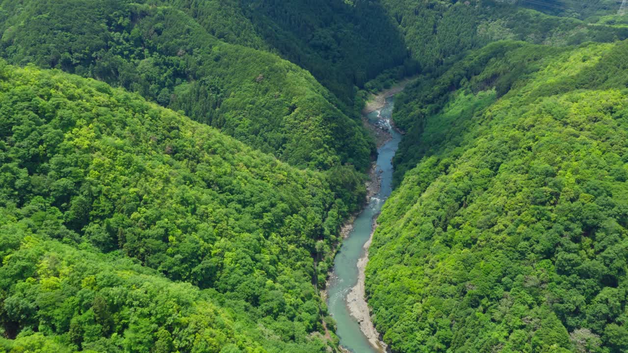 Aerial fly high above Arashiyama river crossing Green lush Mounts of Kyoto Japan landscape