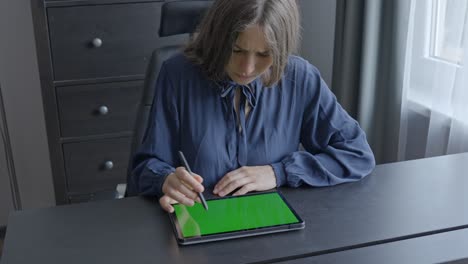 woman is thinking while pointing at her green screen tablet in home office