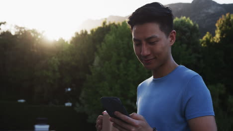 Checking smartphone, asian man drinking morning coffee in casual setting, on balcony, copy space