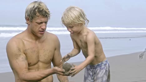 dad throwing sand ball to little son while playing on beach