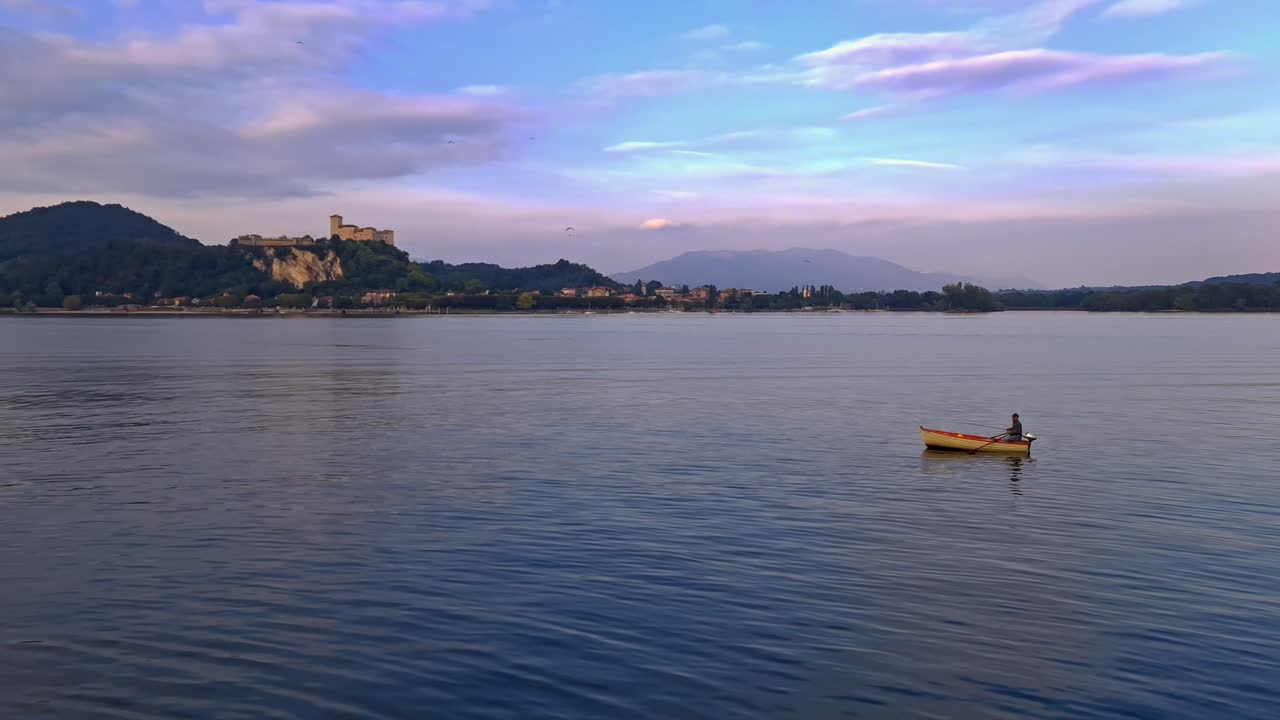 pequeño bote de remos de pesca con pescador a bordo en aguas tranquilas del lago maggiore en italia con gaviota volando por encima