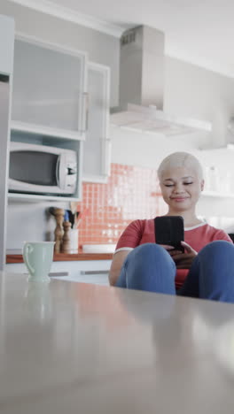 vertical video of happy biracial woman using smartphone and drinking coffee in slow motion