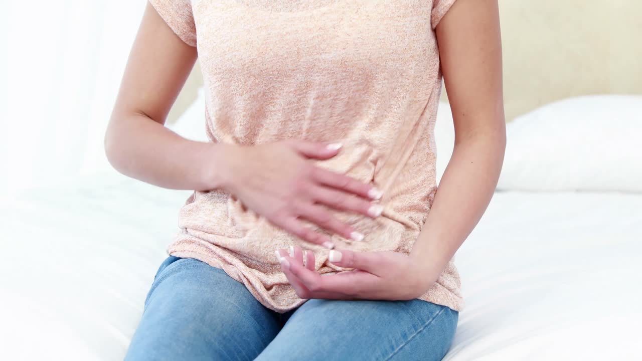 Woman sitting on bed with stomach pain