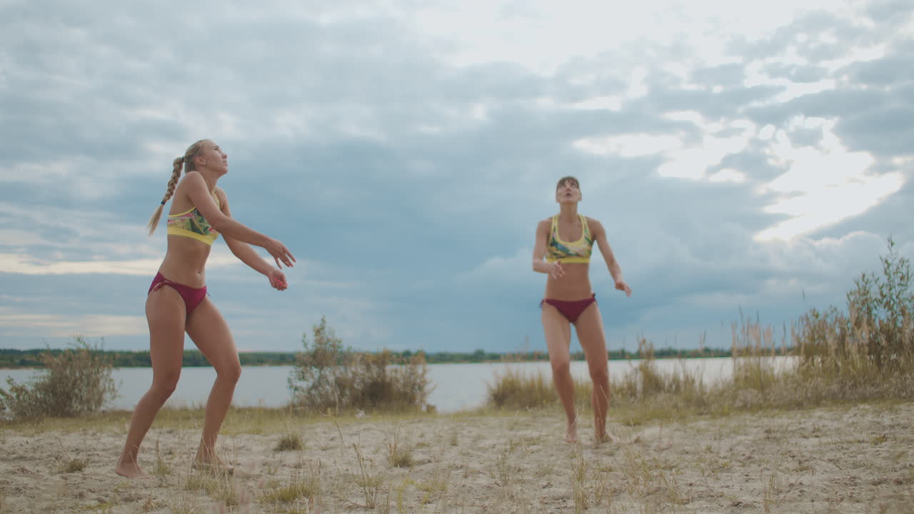 해변 배구 선수 들 은 야외 에서 훈련 하고 있으며, 두 명 의 스포츠 여자 들 이 슬로우 모션 을 통과 하고 공격 하고 있다