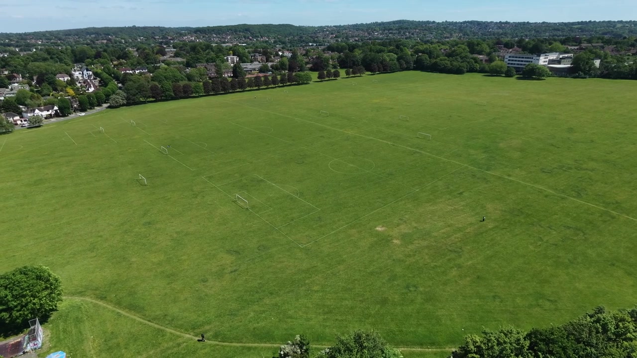 Drone parallax over green sports field, suburban trees and houses in summer.