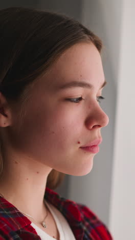 depressed young woman with long brown hair stands looking out of window in light room closeup slow motion. psychotherapy to help change mental state