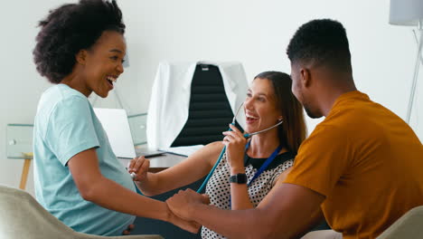 Pregnant-Couple-At-Appointment-With-Female-Doctor-Or-GP-Listening-With-Stethoscope-In-Office