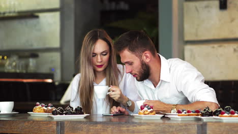 young man pointing on girl's telephone while making booking online and discussing ,male and female colleagues communicating on coffee break checking updated on education web page via smartphone