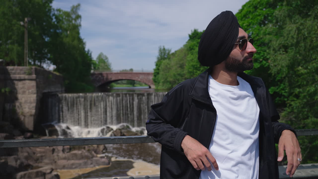 hombre sikh punjabi con gafas de sol y turbante dastar de pie en el puente con vanhankaupunkoski, cascada del casco antiguo en helsinki, finlandia