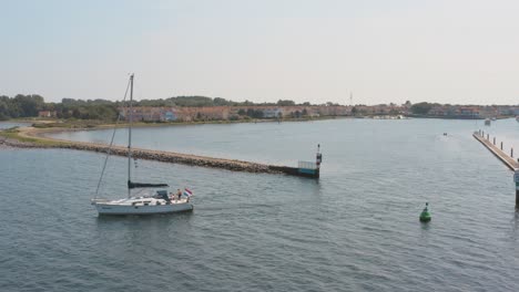 cinematic drone - aerial shot of a boat sailing on the ocean with a marina in the background with sailing boats on a sunny day at zeeland at the north sea, netherlands, 25p