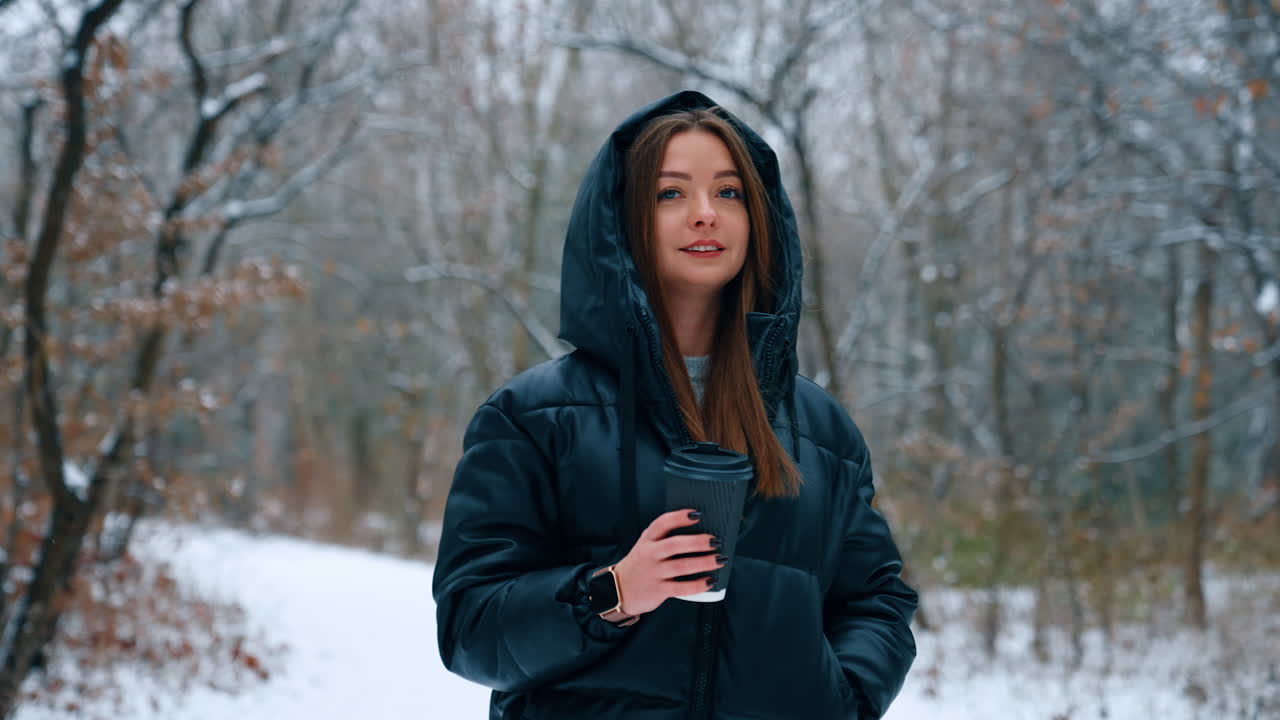 Caucasian long-haired lady in black blazer walking by the park. Woman holds a paper cup and enjoys winter day.